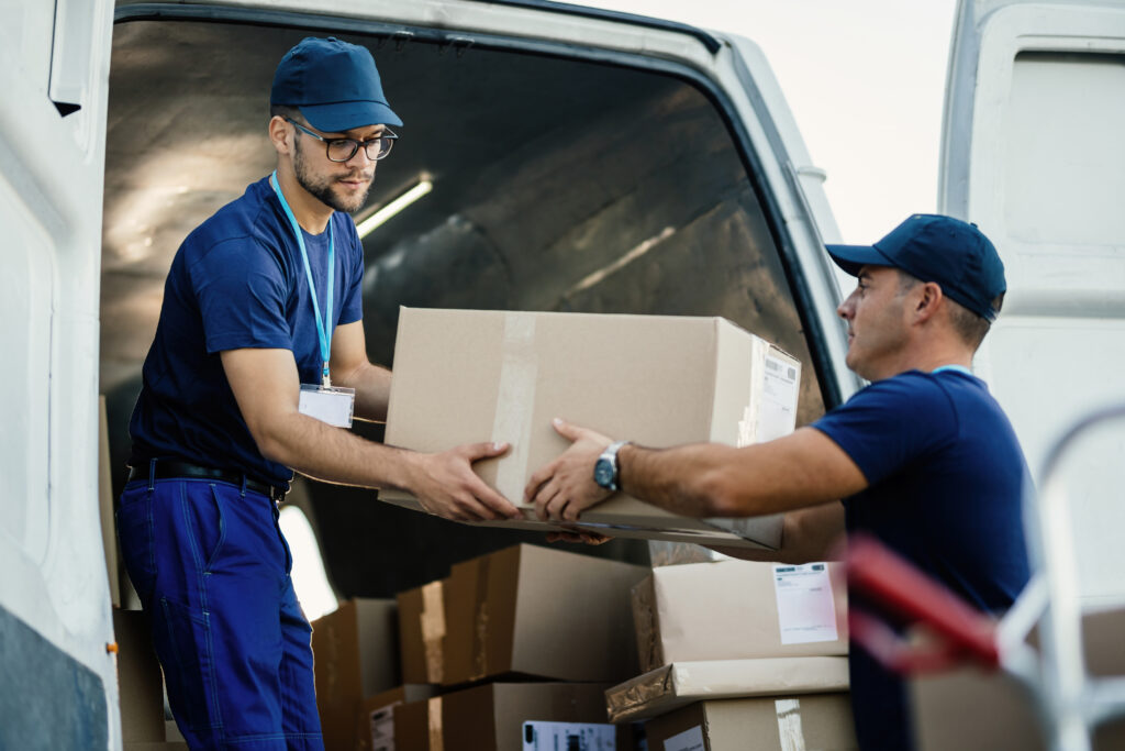 Two movers in blue uniforms loading cardboard boxes into a van during a relocation process.